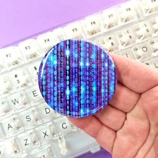 Hand holding a round, blue and purple patterned object over a keyboard with a purple background