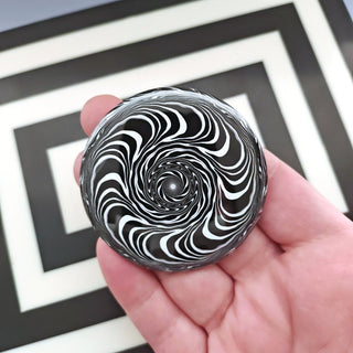 Black and white swirl button held in a hand with geometric background