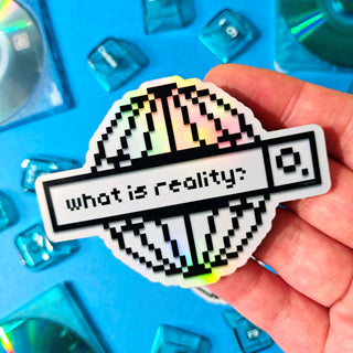 Hand holding a pixelated sticker with 'what is reality?' text against a blue background with transparent objects.