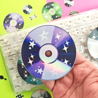 Hand holding a CD with star design over a keyboard with colorful CDs in the background
