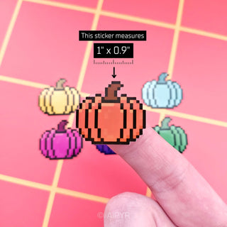 Pixelated pumpkin sticker being held by a finger on a pink grid background, with measurement text overlay.