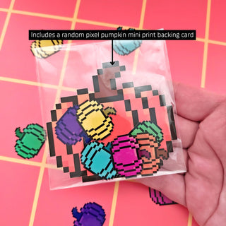 Pixelated pumpkin mini print card held by a hand with text on a pink grid background