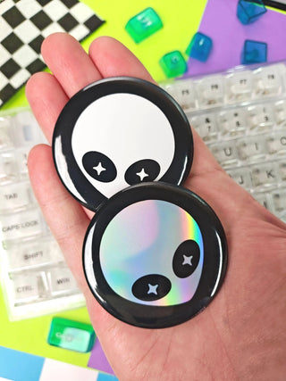 Two round, cartoonish phone accessories held in a hand with a keyboard in the background.