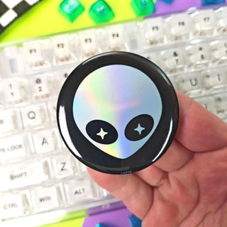 Hand holding a round, iridescent object with alien face design on a colorful keyboard background