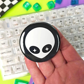 Hand holding a round object with an alien face design over a colorful keyboard background
