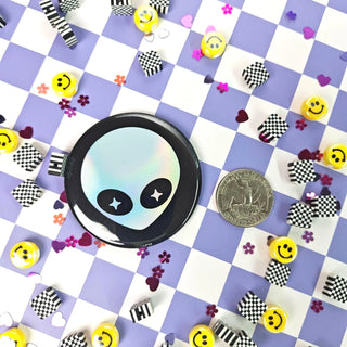 Circular button with alien design on a checkered background with decorative items