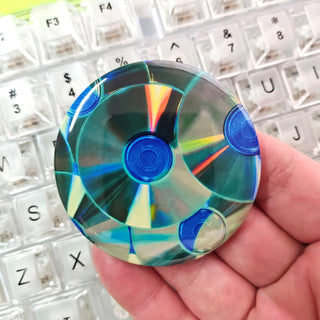 Colorful blue button held in a hand with a keyboard in the background