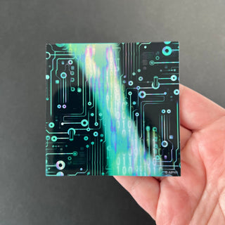 Blue Matrix Glitch Holographic Sticker by AIPYR laying on a human hand over a black background.