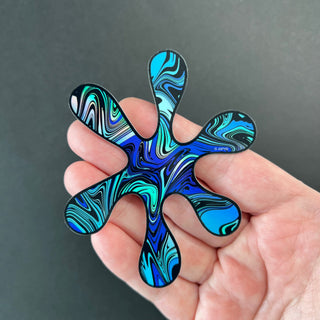 Blue Swirl Splat Holographic Sticker by AIPYR laying on a human hand over a black background.