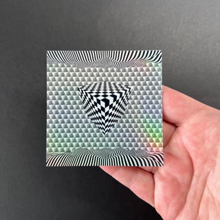 Cube Illusion Holographic Sticker by AIPYR laying on a human hand over a black background.