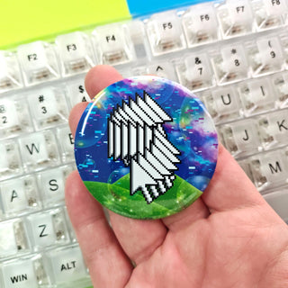 Button badge with a pixelated design held in front of a keyboard