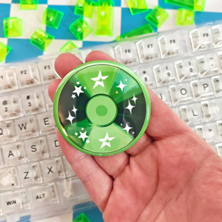 Hand holding a green cd button with star patterns in front of a keyboard.