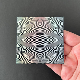 Hypnotic Wave Holographic Sticker by AIPYR laying on a human hand over a black background.