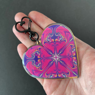 Psychedelic Pink Heart Keychain by AIPYR laying flat on a human hand over a black background.