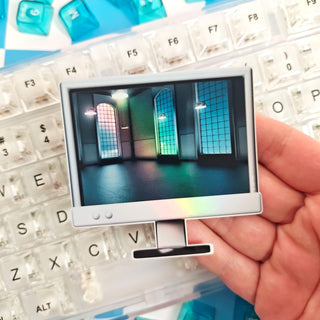 Hand holding a small computer monitor with a colorful display in front of a keyboard