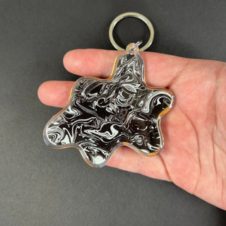 Monochrome Chaos Blob Keychain by AIPYR laying on a human hand over a black background.