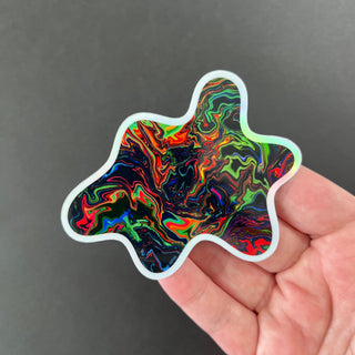 Neon Chaos Holographic Sticker by AIPYR laying on a human hand over a black background.