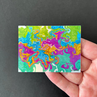 Neon Fluid Swirl Holographic Sticker by AIPYR laying on a human hand over a black background.