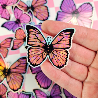 Holographic butterfly sticker held by a hand with a colorful butterfly pattern in the background