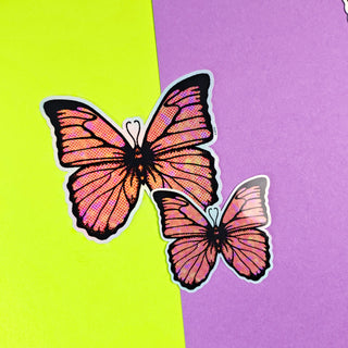 Two orange butterfly stickers on a purple and green background
