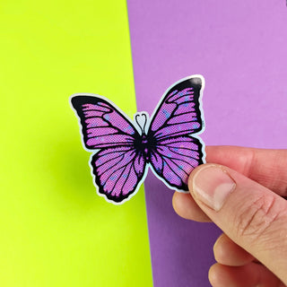 Hand holding a purple butterfly sticker against a purple and green background
