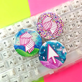Three colorful pixelated mouse cursor pinback buttons on a clear keyboard with a pink and green background