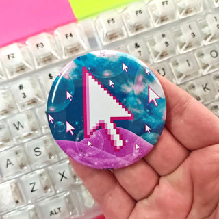 Button badge with pixelated cursor design held over a keyboard