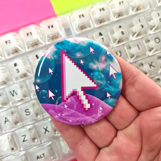 Button badge with pixelated cursor design held over a keyboard