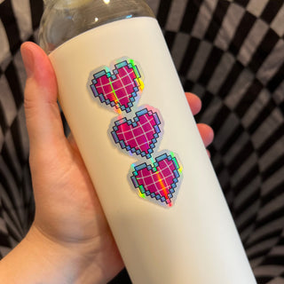 Pixelated Hearts Holographic Sticker by AIPYR shown in use on a white glass water bottle.