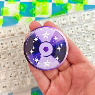 Hand holding a purple cd button with star design on a keyboard background