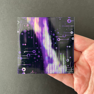 Purple Matrix Glitch Holographic Sticker by AIPYR laying on a human hand over a black background.