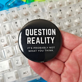 Hand holding a 'Question Reality' button over a colorful keyboard