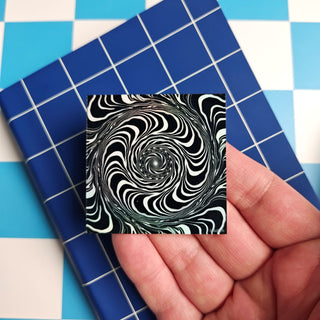 Black and white spiral design on a small square card held over a blue and white checkered background.