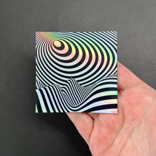 Trippy Op Art Landscape Holographic Sticker by AIPYR laying on a human hand over a black background.