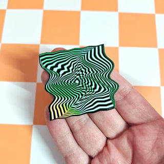 Hand holding a green and black wavy patterned object against an orange and white checkered background