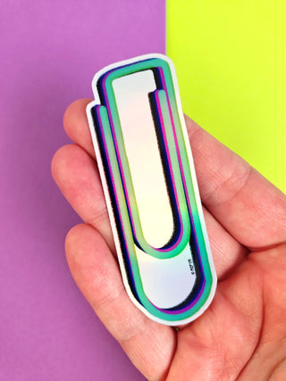 Colorful U-shaped paper clip held in a hand against a purple and green background