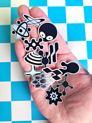 Hand holding black and white molecular structure stickers on a blue and white checkered background